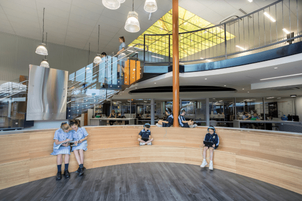 A large open two level indoor learning space. A large staircase leads up to a mezzanine area, and a large lower level is fitted out with curved timber seating.