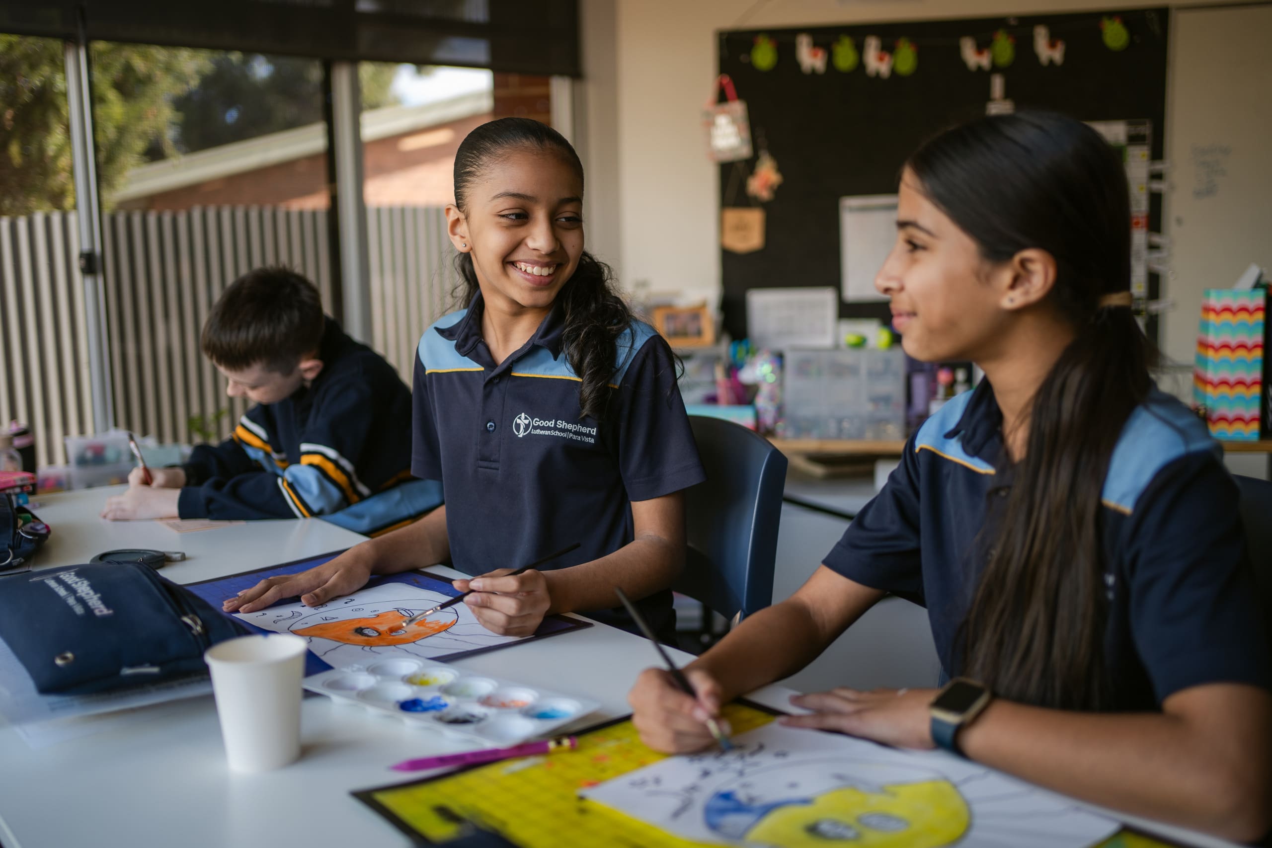 Students sitting at a desk. They are smiling.