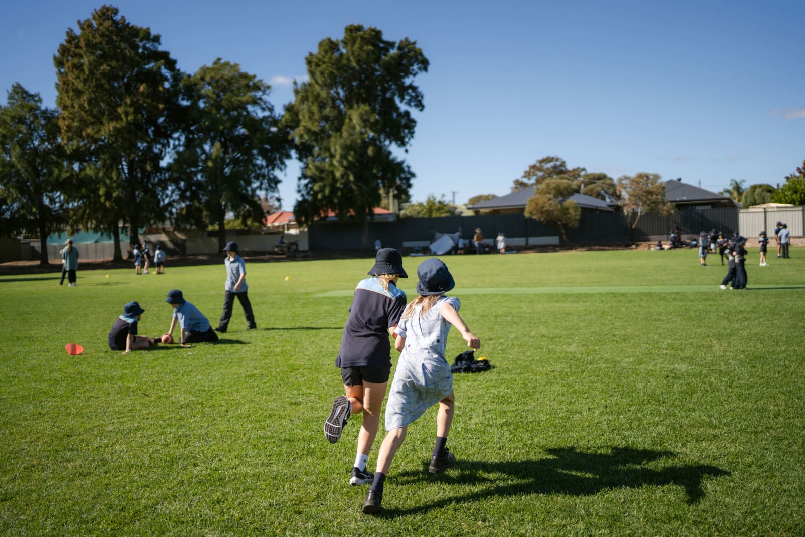 Two students are on the school oval. They are running away from the camera.