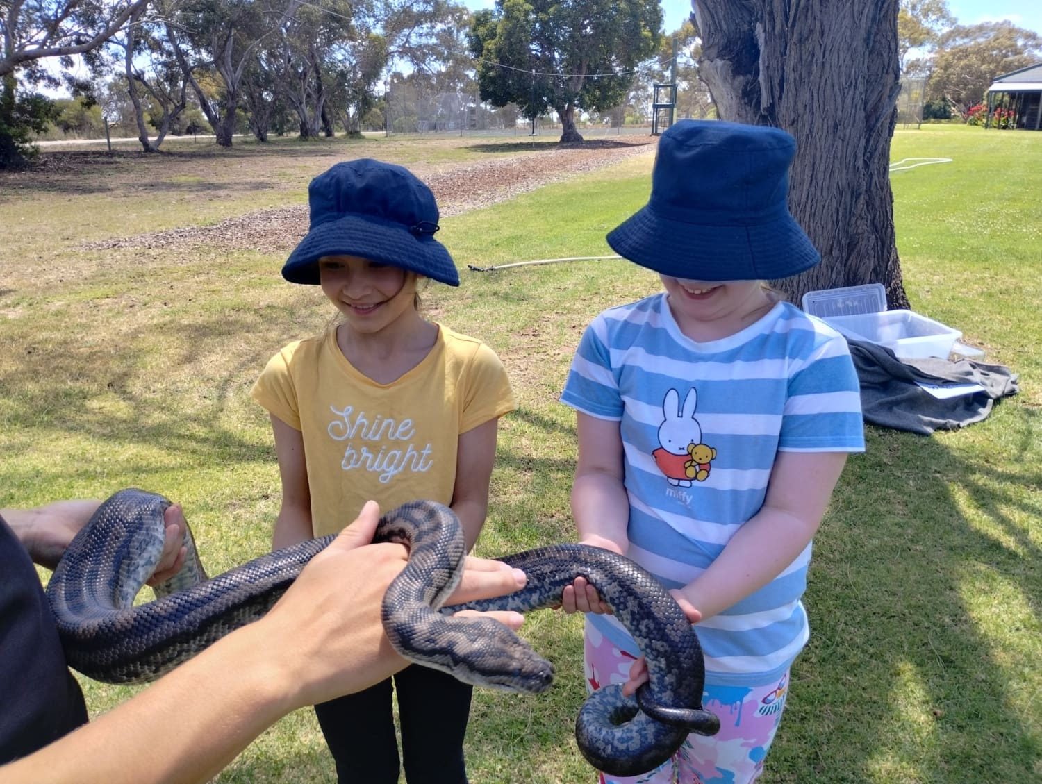 Two young students are standing together outside. They are holding a large python while on school camp.