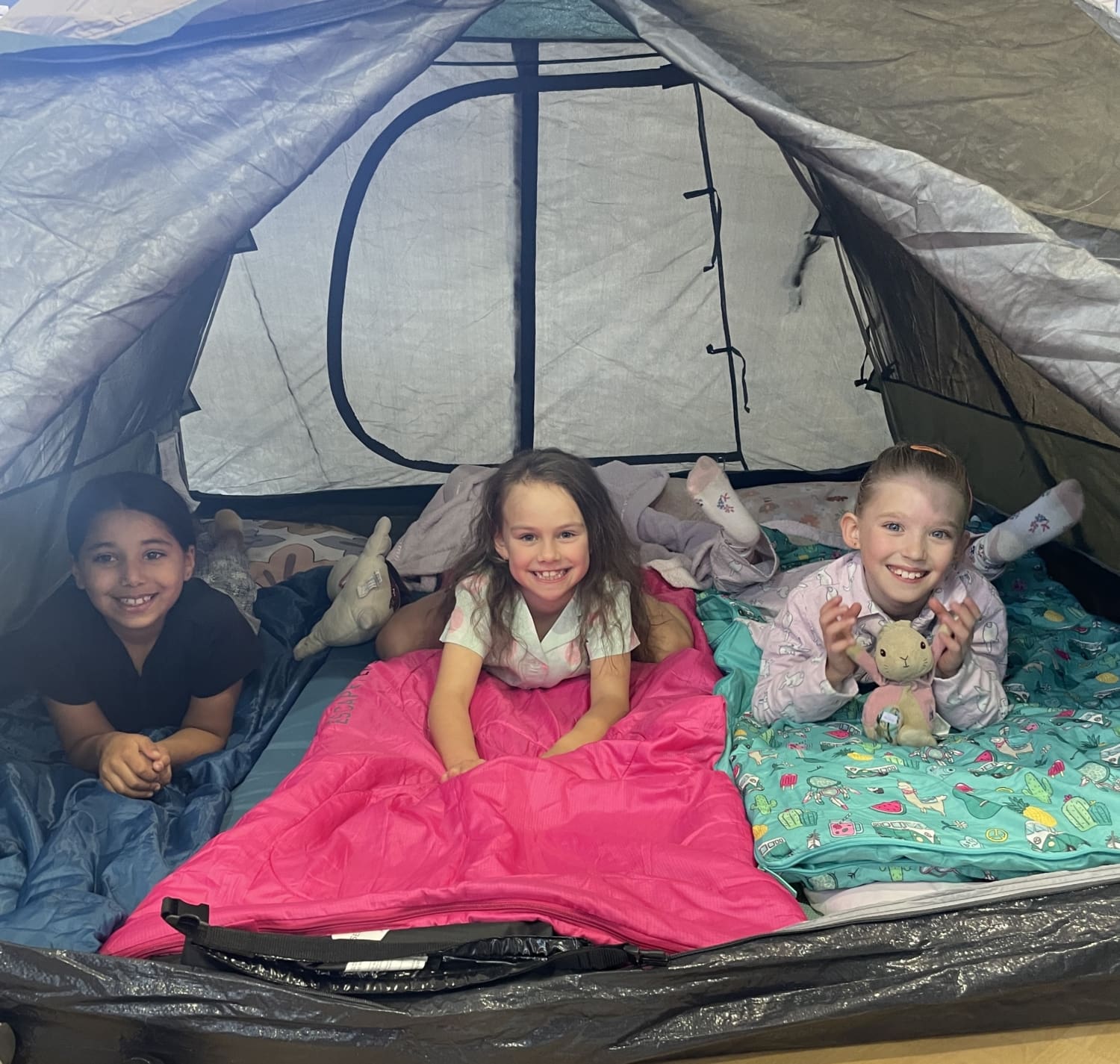 Three young students are in a tent and smiling at the camera.