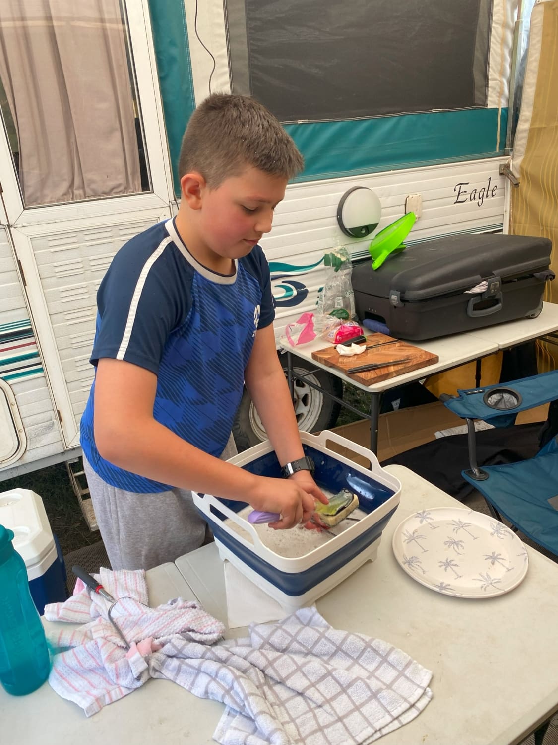 A young male student on school camp is pictured washing dishes in a little tub.