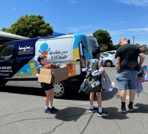 Two students help a man from a charity load a van with donated goods.
