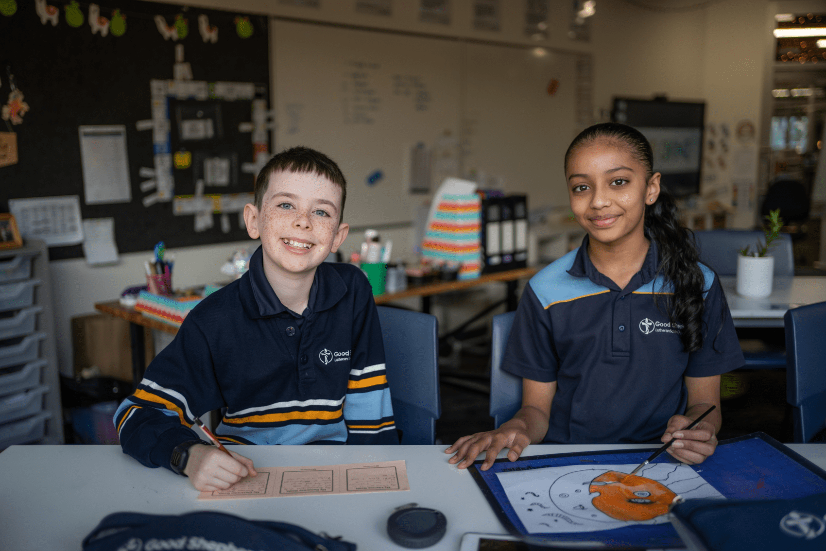 Two primary school students from Good Shepherd Lutheran School are in a classroom sitting at a desk. They are looking at the camera and smiling.