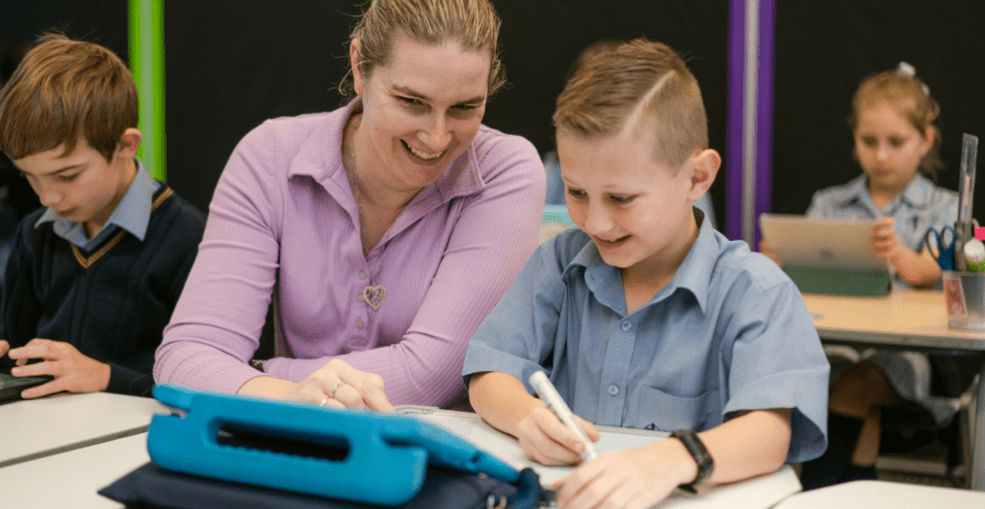 A teacher is working with a student. They are both smiling. They are using Technology in the classroom.